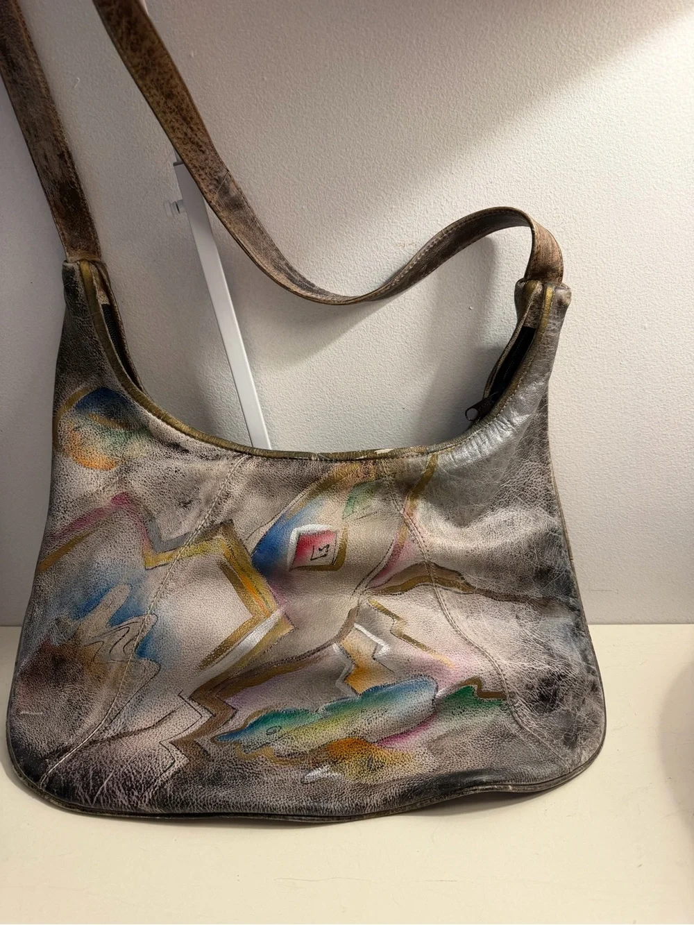 Distressed leather hobo bag with colorful abstract design on front and back.